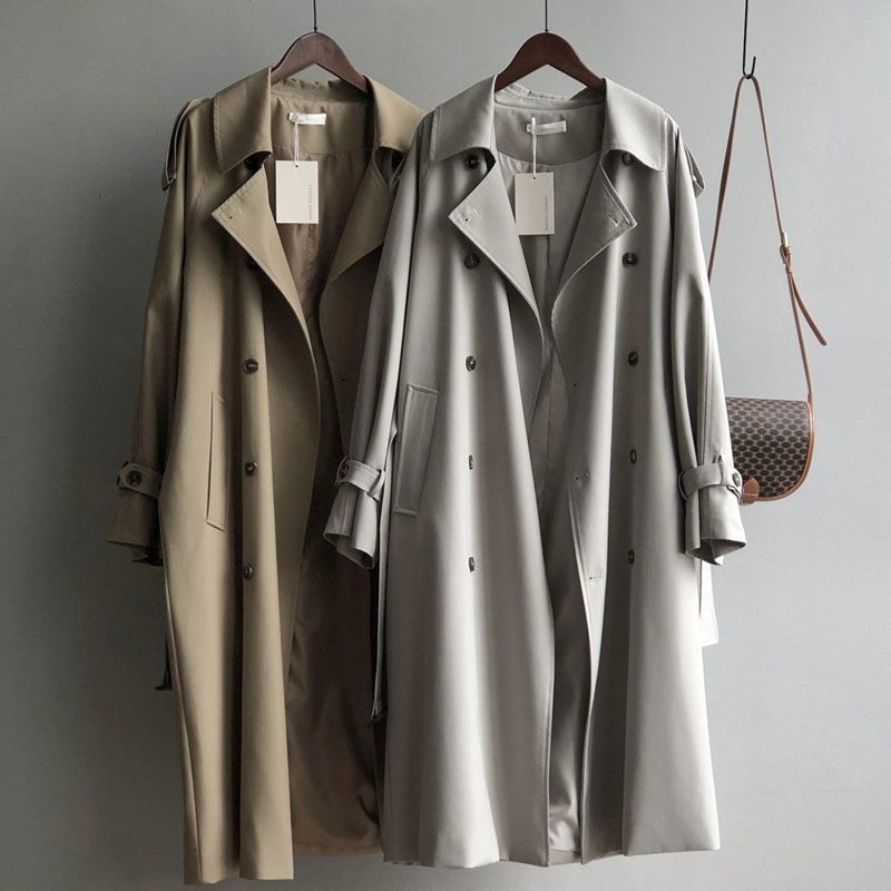 Two trench coats hanging side by side on a gray background